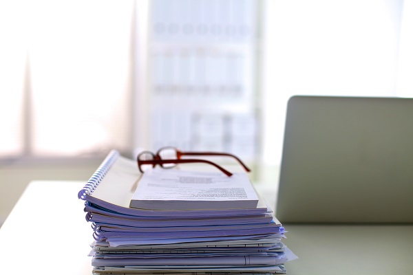 EMC photo of a stack of papers and note books with glasses on the top of the pile